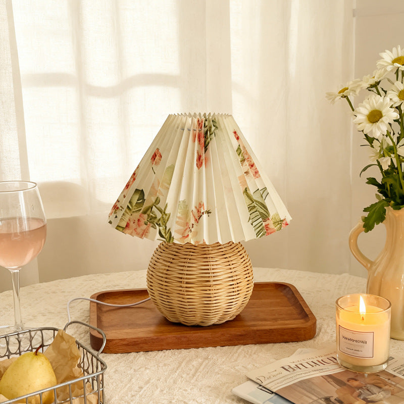 Floral-patterned lampshade on a wicker base with a candle and flowers on a table.