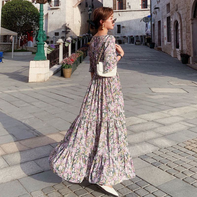 Woman in a floral dress walking down a sunlit street.