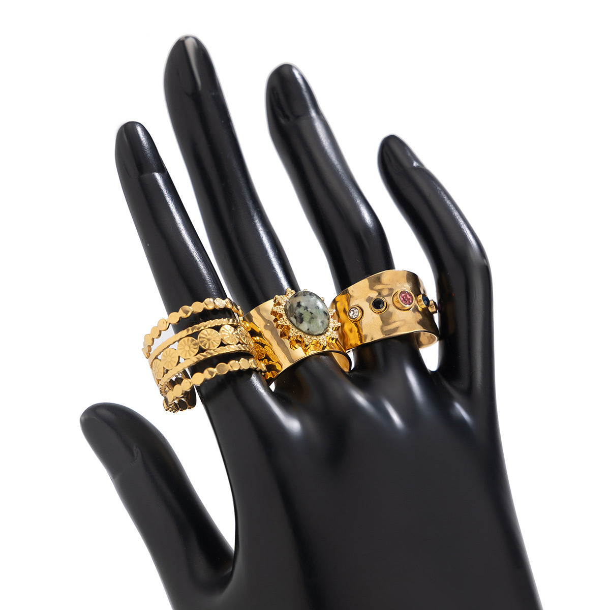 Gold rings with gemstones on a black mannequin hand against a white background