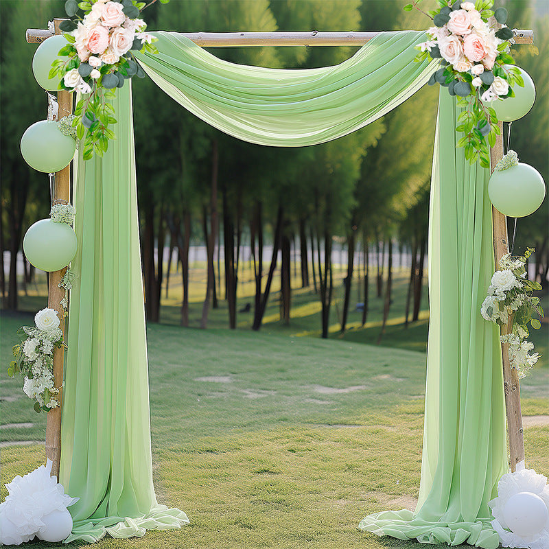 Decorative arch with green fabric, flowers, and balloons in a park setting