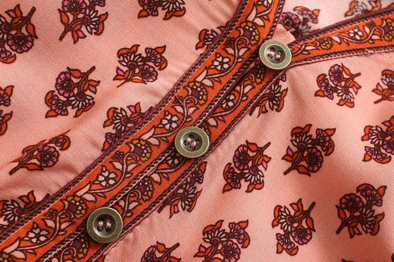 Close-up of a pink fabric with orange floral patterns and metal buttons.