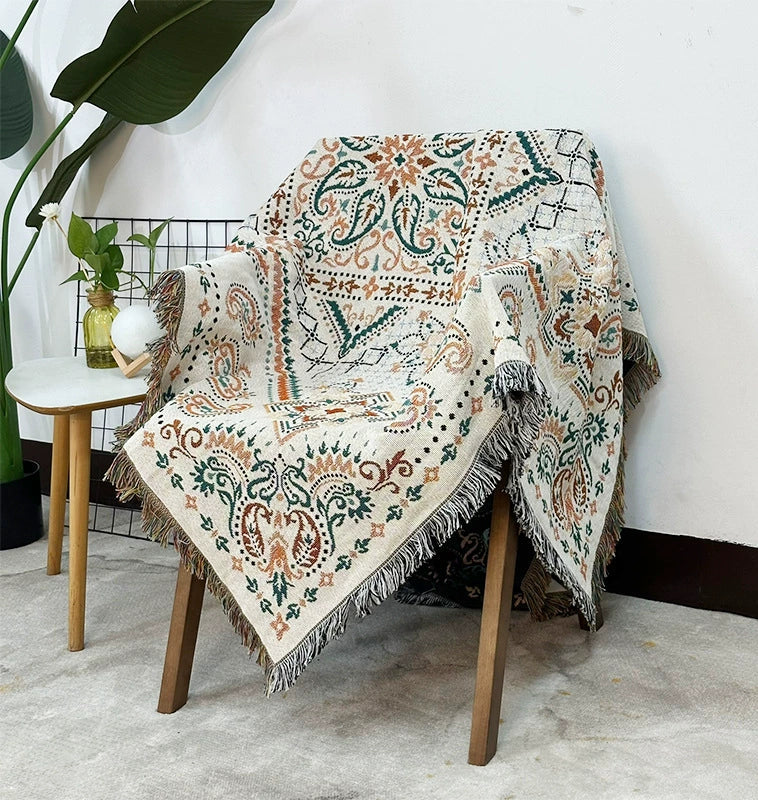 Decorative patterned throw blanket draped over a chair in a room with a plant and small table.