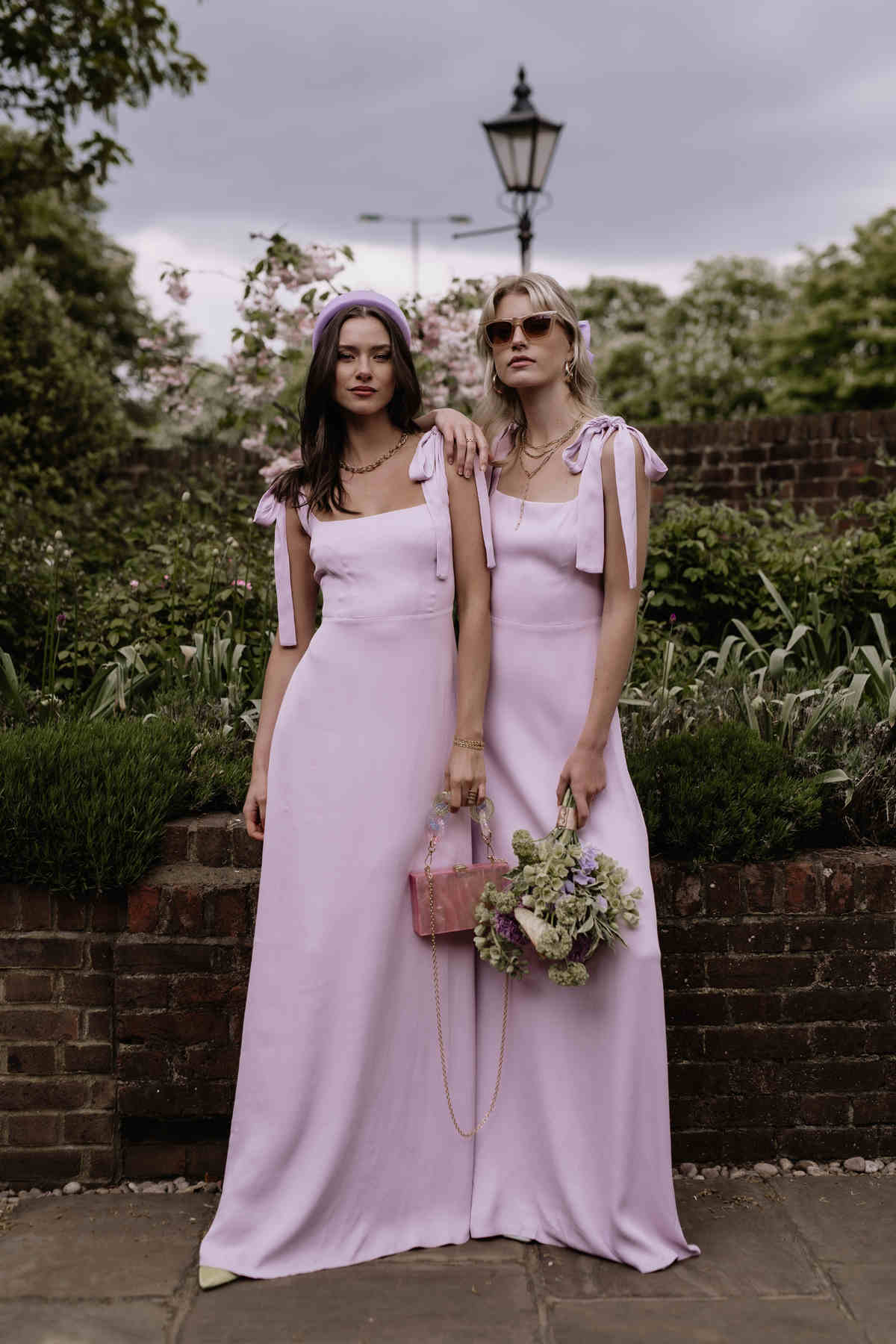 Two women in matching pink dresses standing outdoors with a garden background.