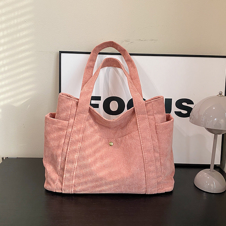 Pink corduroy tote bag on a dark surface with a blurred background