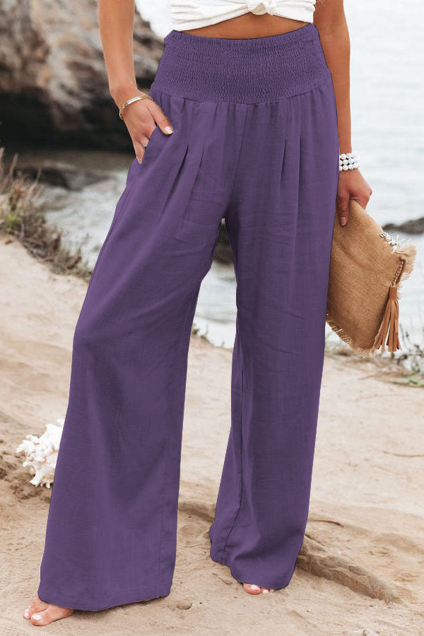 Person wearing purple wide-leg pants by a rocky shoreline