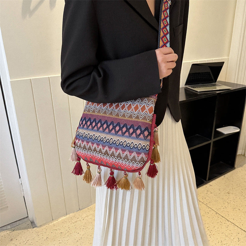Person holding a colorful patterned bag with tassels indoors.