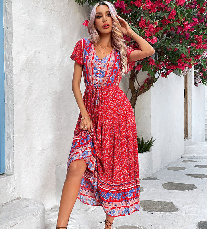 Woman in a red and blue patterned dress standing in front of a white wall with pink flowers.