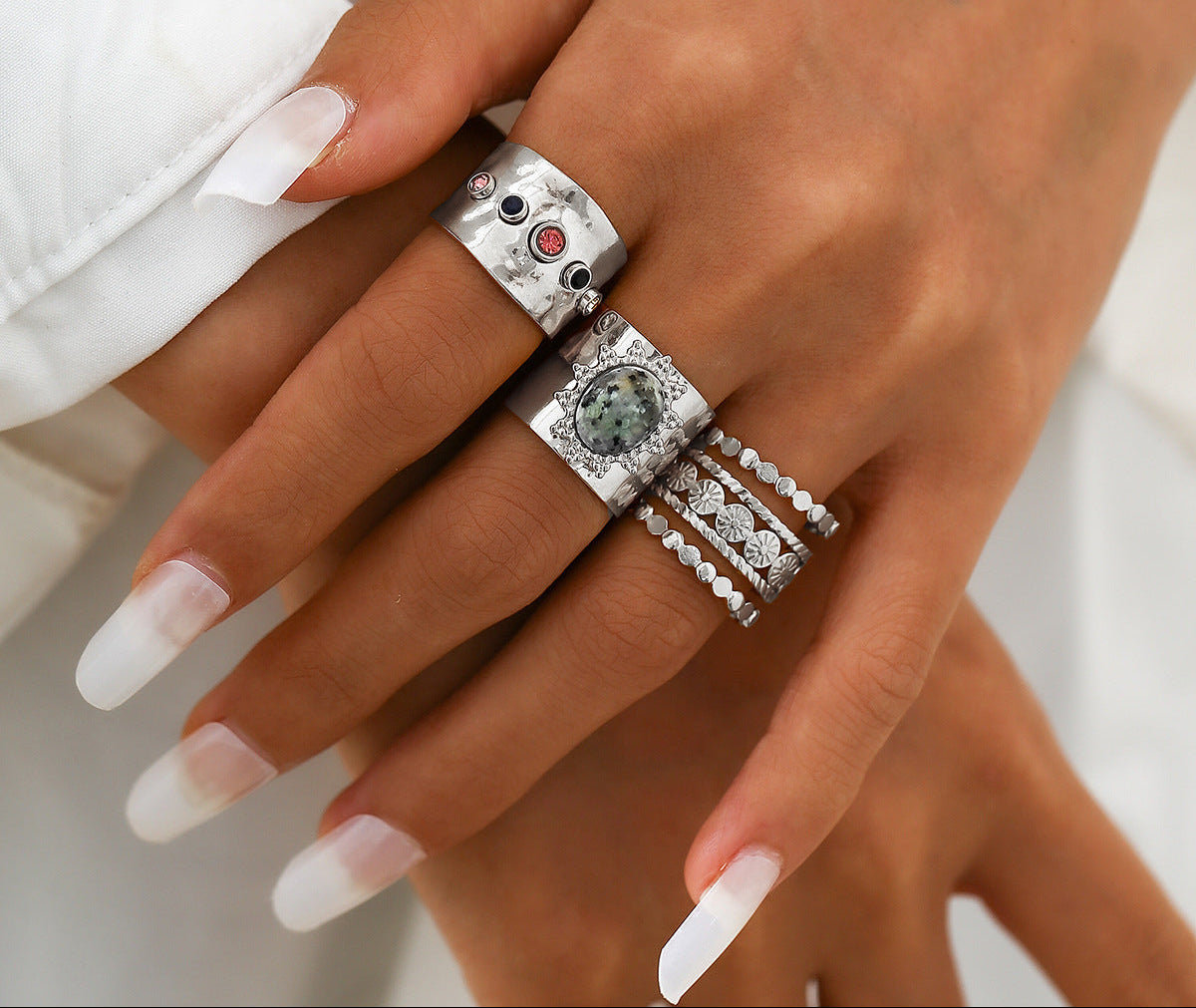 Hand wearing multiple silver rings with gemstones on a neutral background