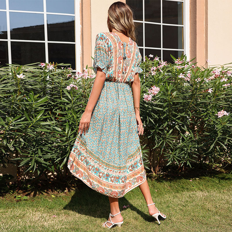 Woman in a floral dress standing outdoors with greenery and a building in the background