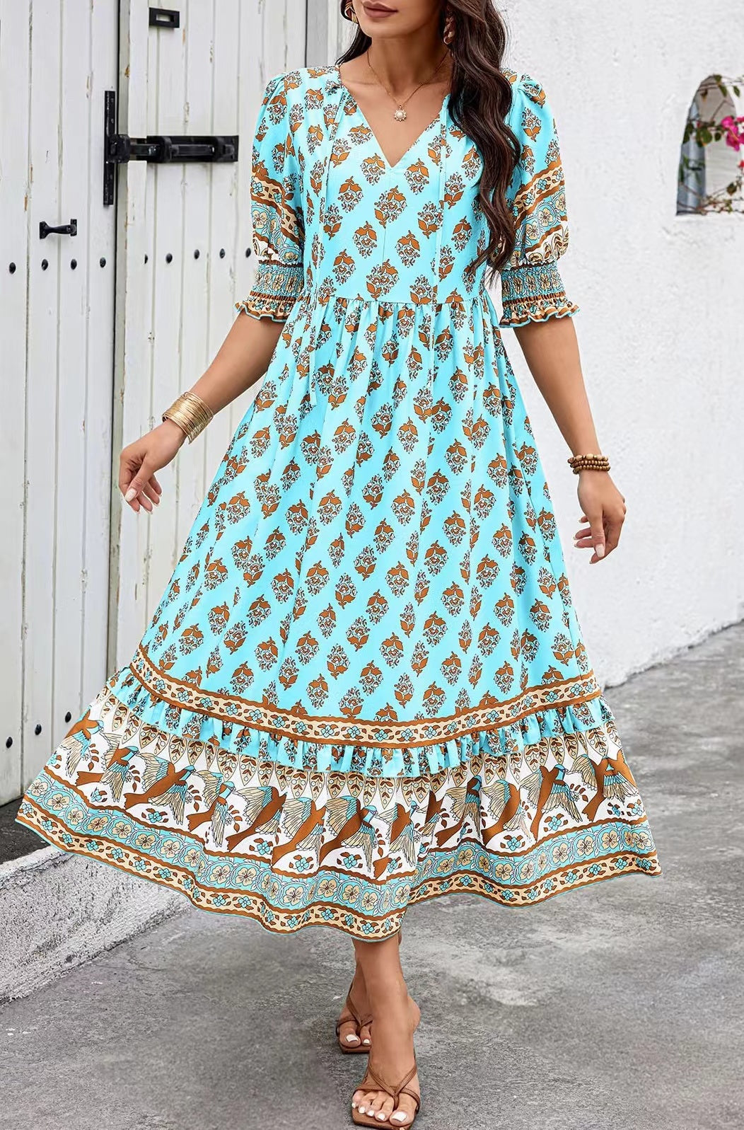 Woman wearing a blue patterned dress standing against a white wall.
