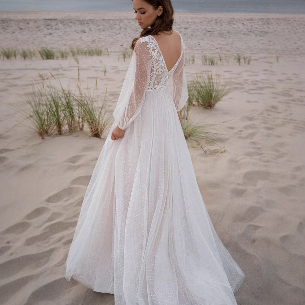 Woman in a white lace bridal dress standing on a sandy beach.