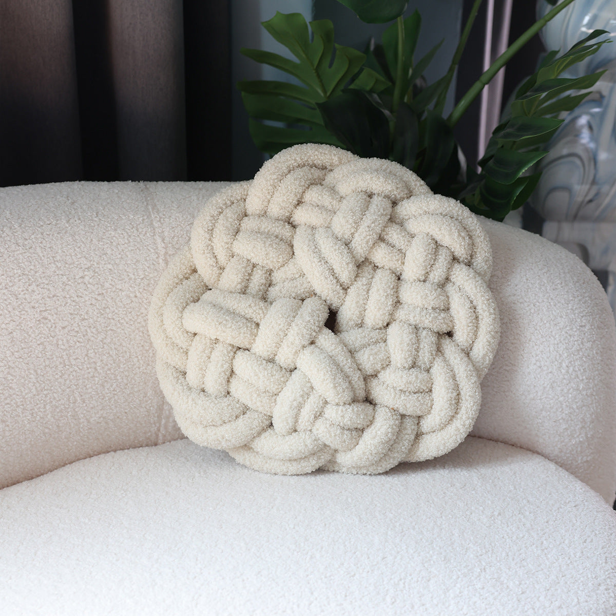 Decorative knot pillow on a beige armchair with a plant in the background