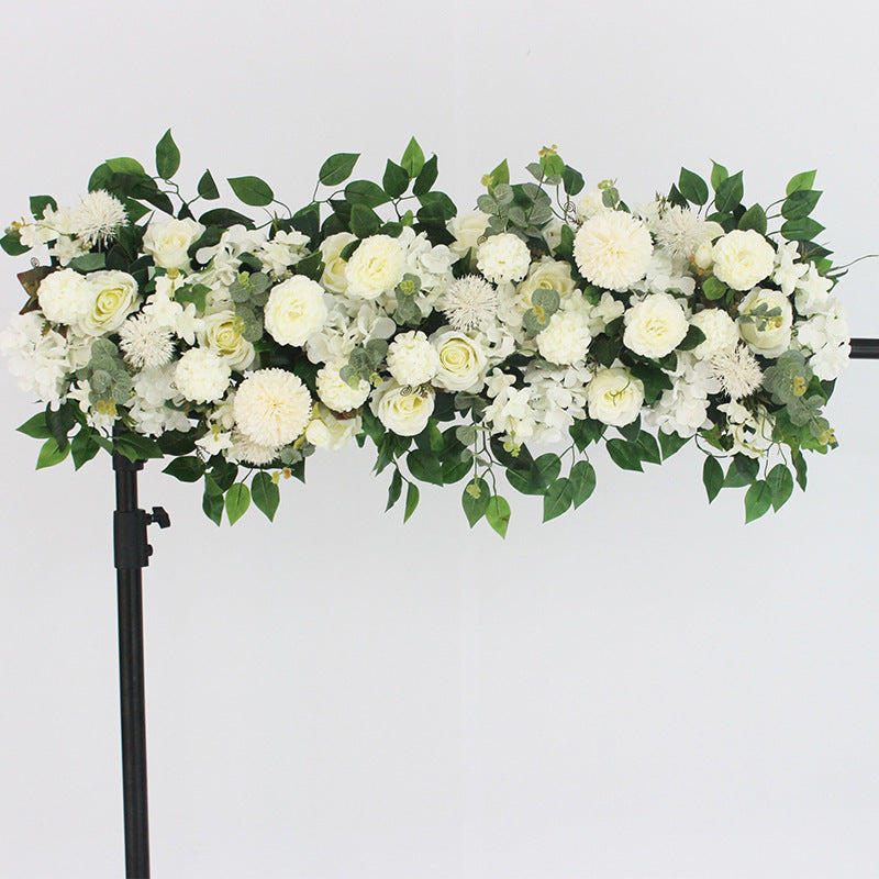 Floral arrangement with white flowers and green leaves on a stand against a light gray background
