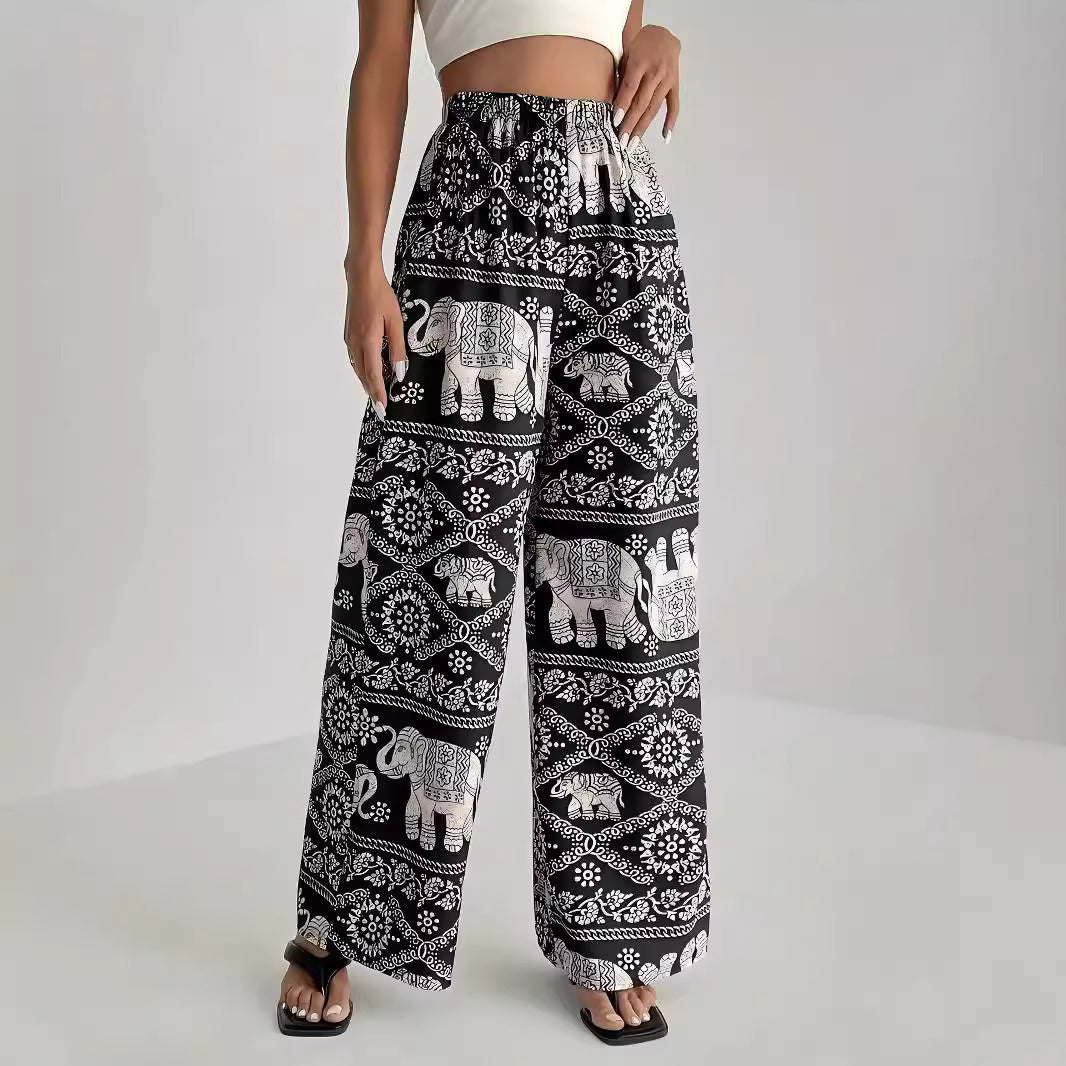 Black wide-leg pants with white elephant pattern worn by a person on a white background