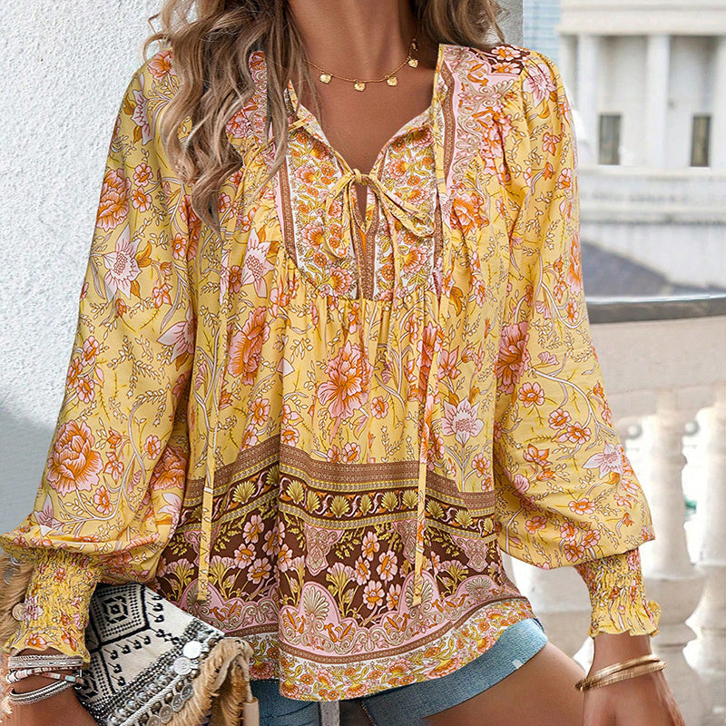 Woman wearing a yellow floral blouse with long sleeves, standing outdoors.