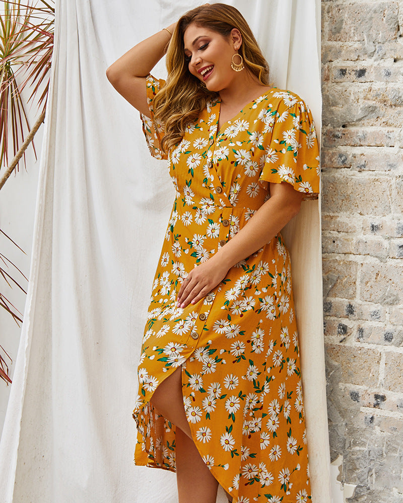 Woman wearing a yellow floral dress against a stone wall and white curtain background