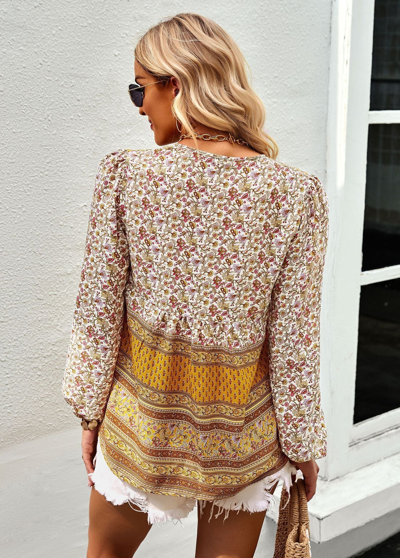 Woman wearing a floral blouse and yellow patterned skirt standing against a light gray wall.