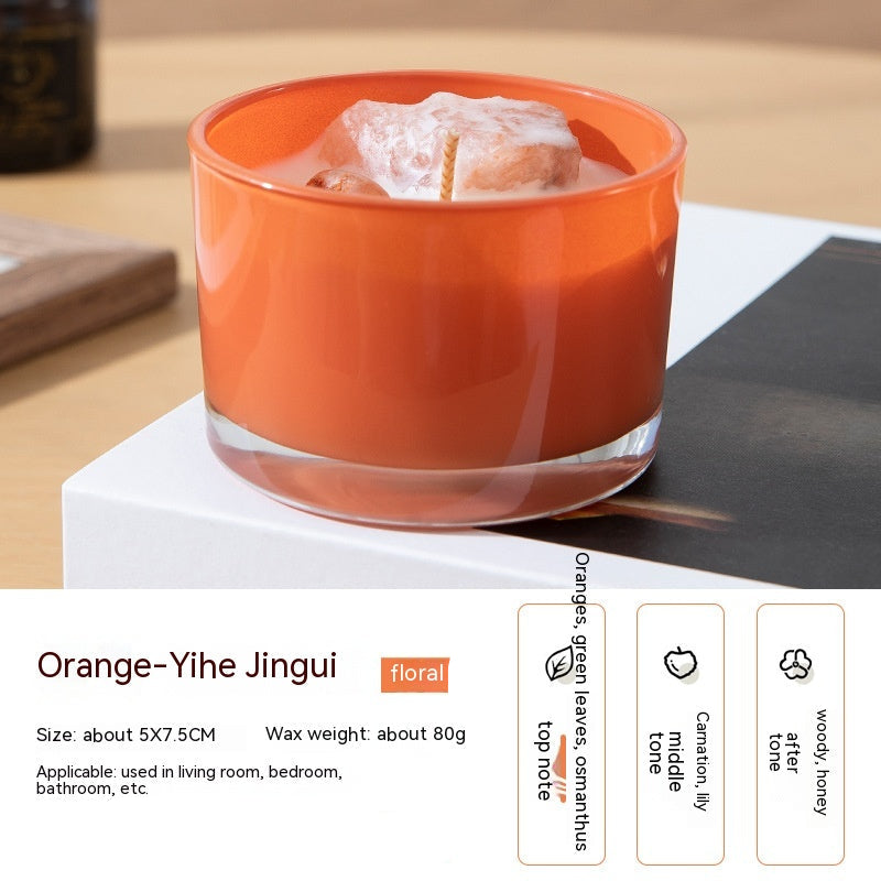 Orange candle in a glass container on a white surface with product details.
