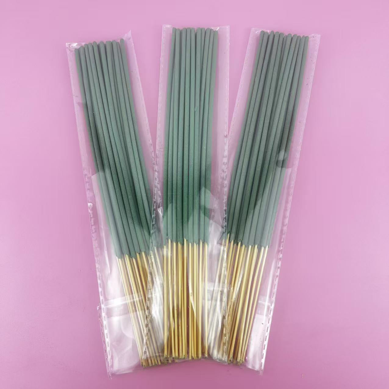Three packages of green incense sticks with gold tips on a pink background