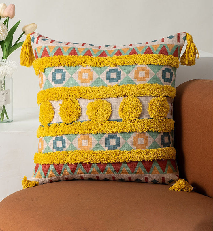 Decorative pillow with geometric pattern and tassels on a brown couch, with flowers in the background.