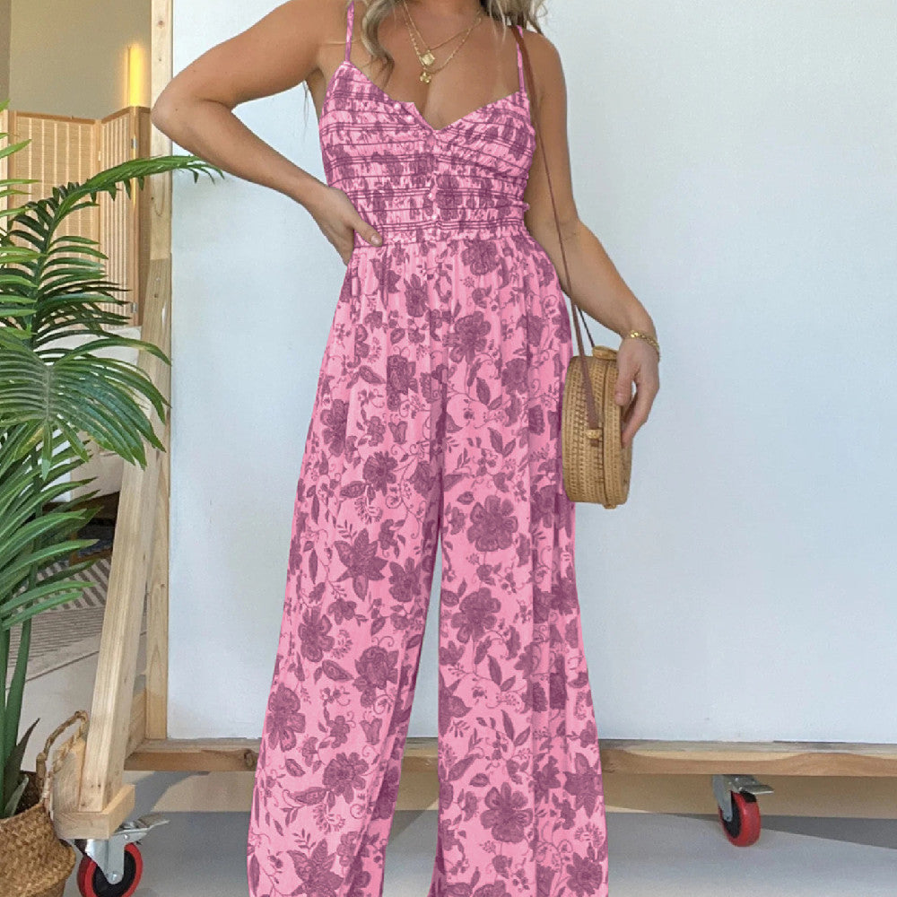 Woman wearing a pink floral jumpsuit holding a woven bag indoors.