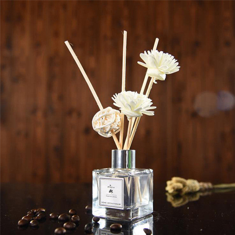 A clear diffuser bottle with floral reeds on a wooden surface.