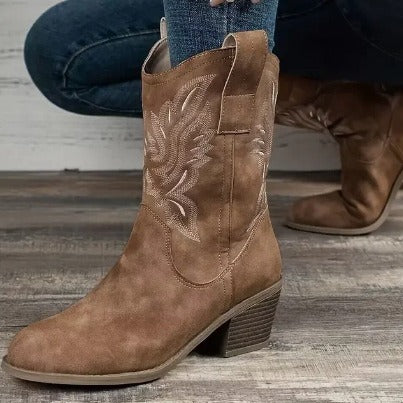 Brown cowboy boot with intricate embroidery on a wooden floor.