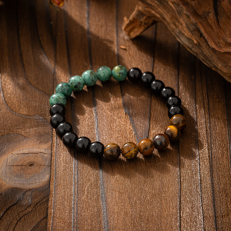 Beaded bracelet with black, green, and brown beads on a wooden surface