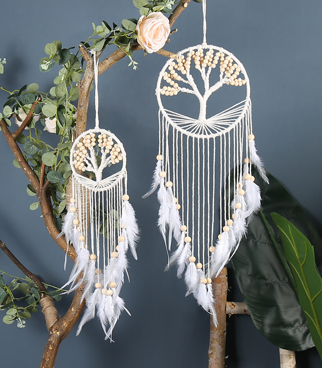 Two white dreamcatchers with tree designs hanging on a branch against a dark background.
