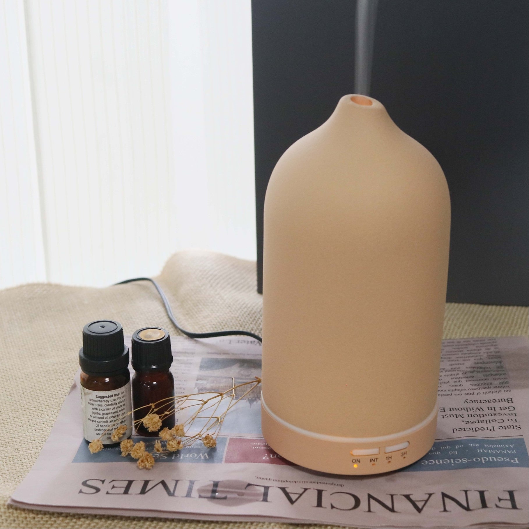 Beige essential oil diffuser on a newspaper with two bottles and dried flowers