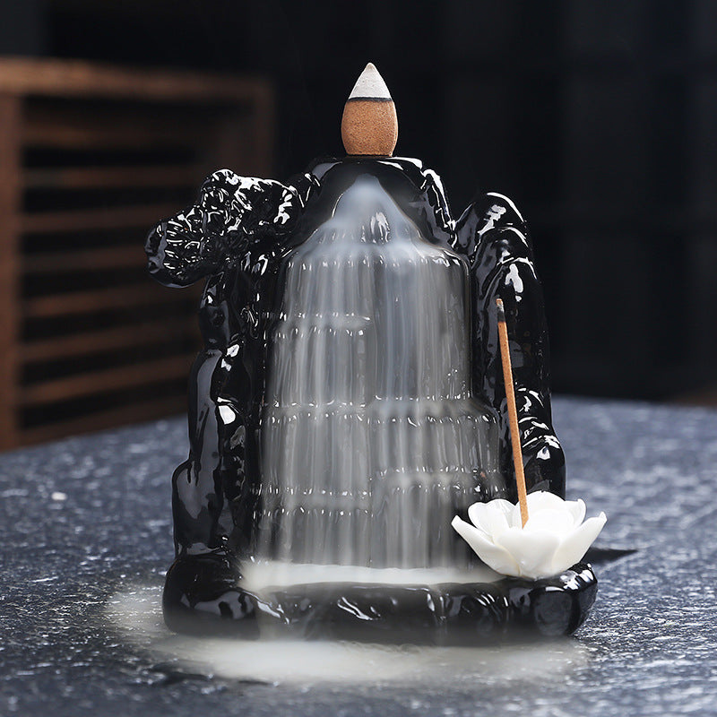 Black incense burner shaped like a waterfall with a white lotus flower on a dark surface.
