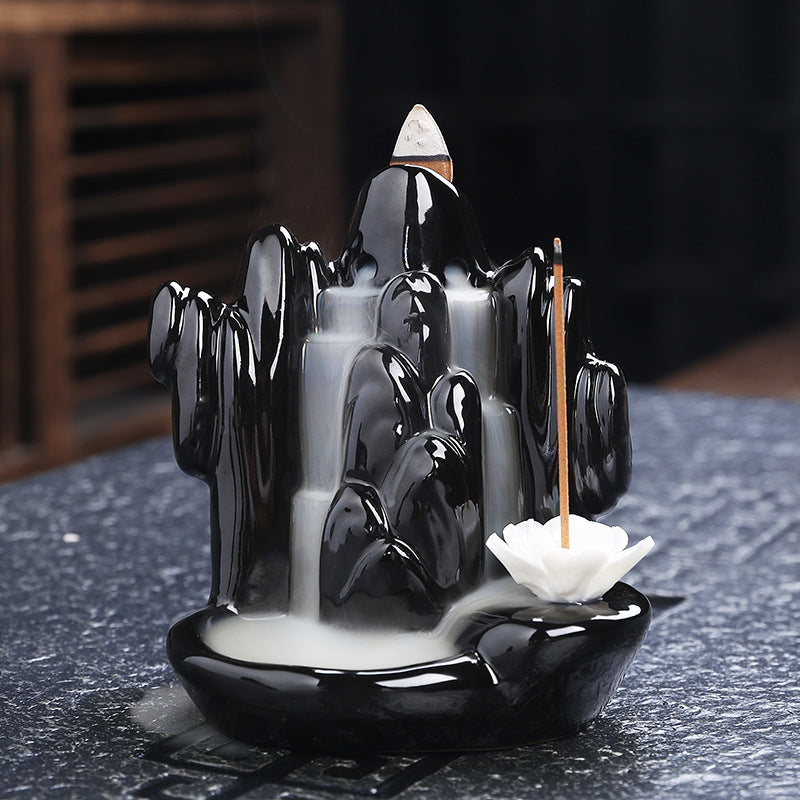 Black mountain-shaped incense burner with white flowers and incense sticks on a dark surface.