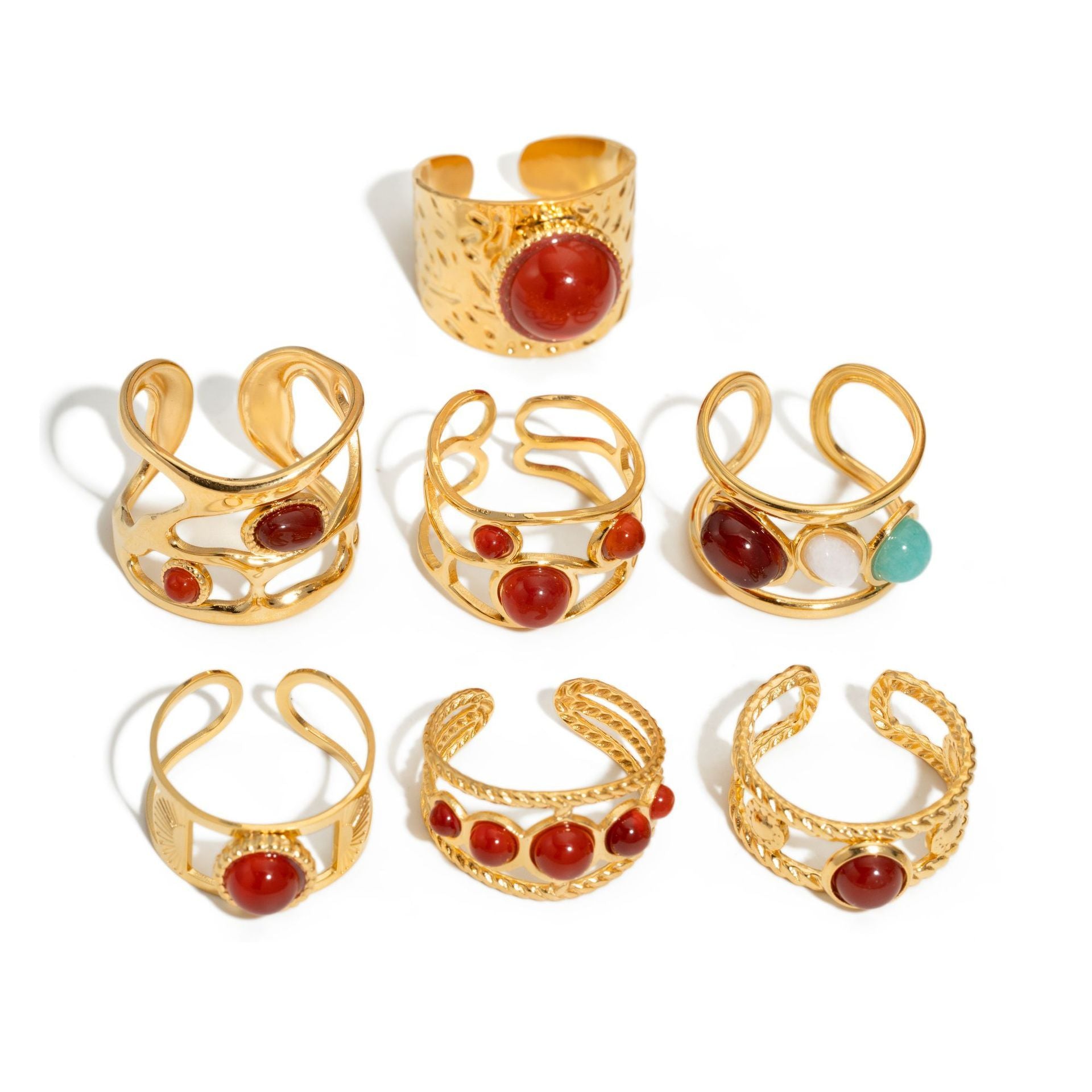 Set of gold rings with red and green gemstones on a white background