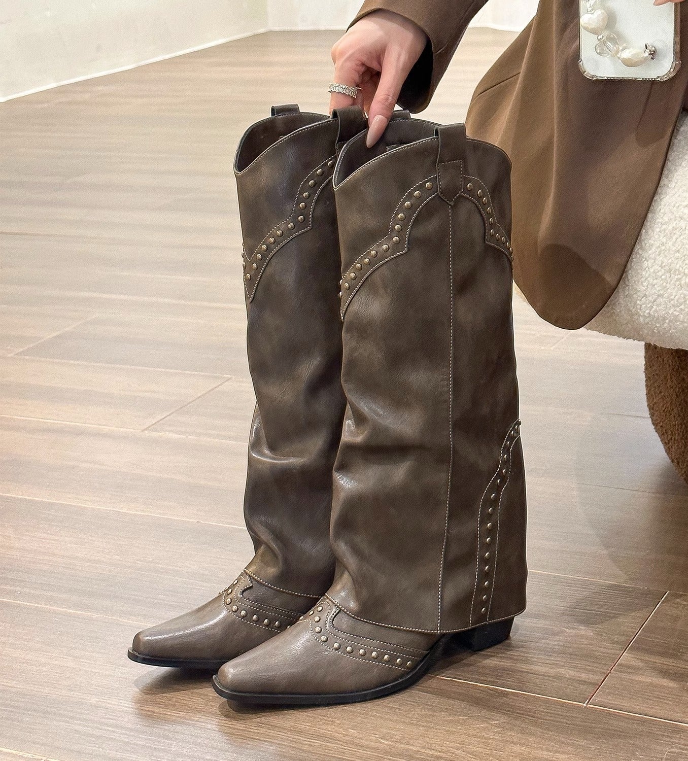 Brown leather boots with decorative studs worn by a person on a wooden floor.