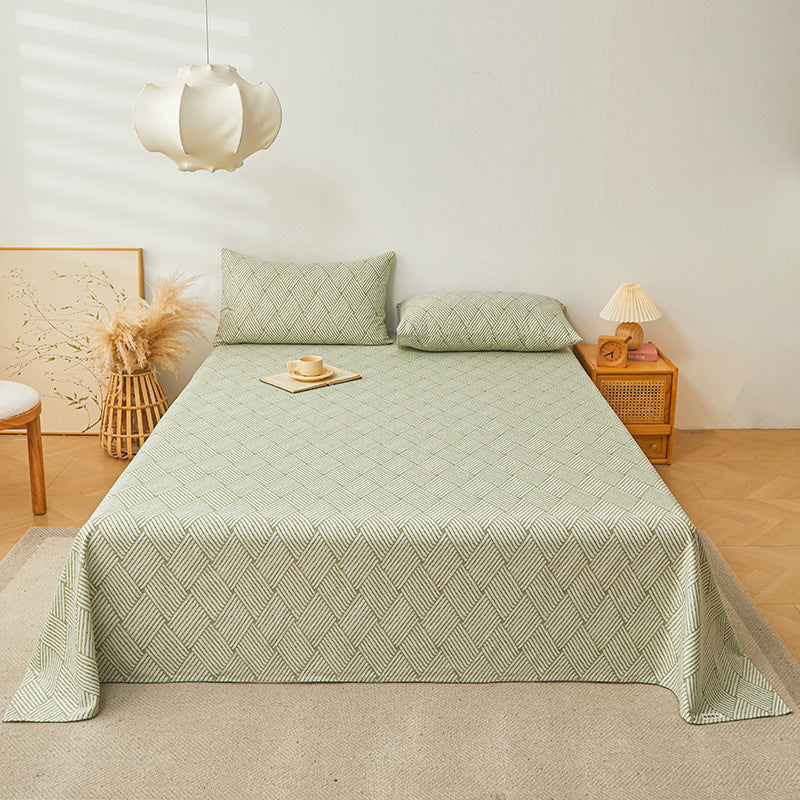 Bed with green patterned bedding in a room with a lamp and decor items.