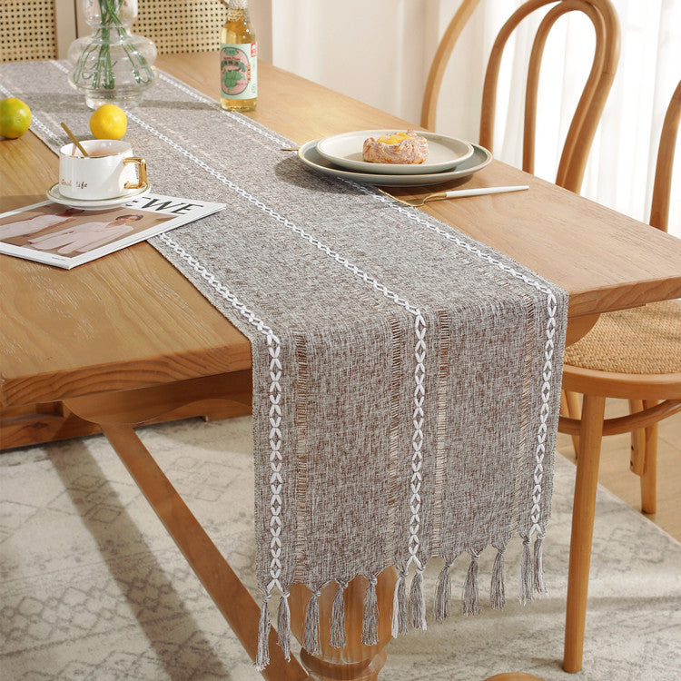Table runner with fringe on a wooden table with a cup, plate, and lemon.