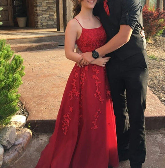Man and woman posing in front of a house, man in black suit and red tie, woman in red dress.