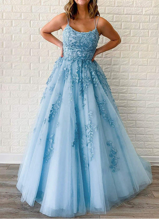 Woman wearing a light blue evening gown with floral details against a white brick wall.