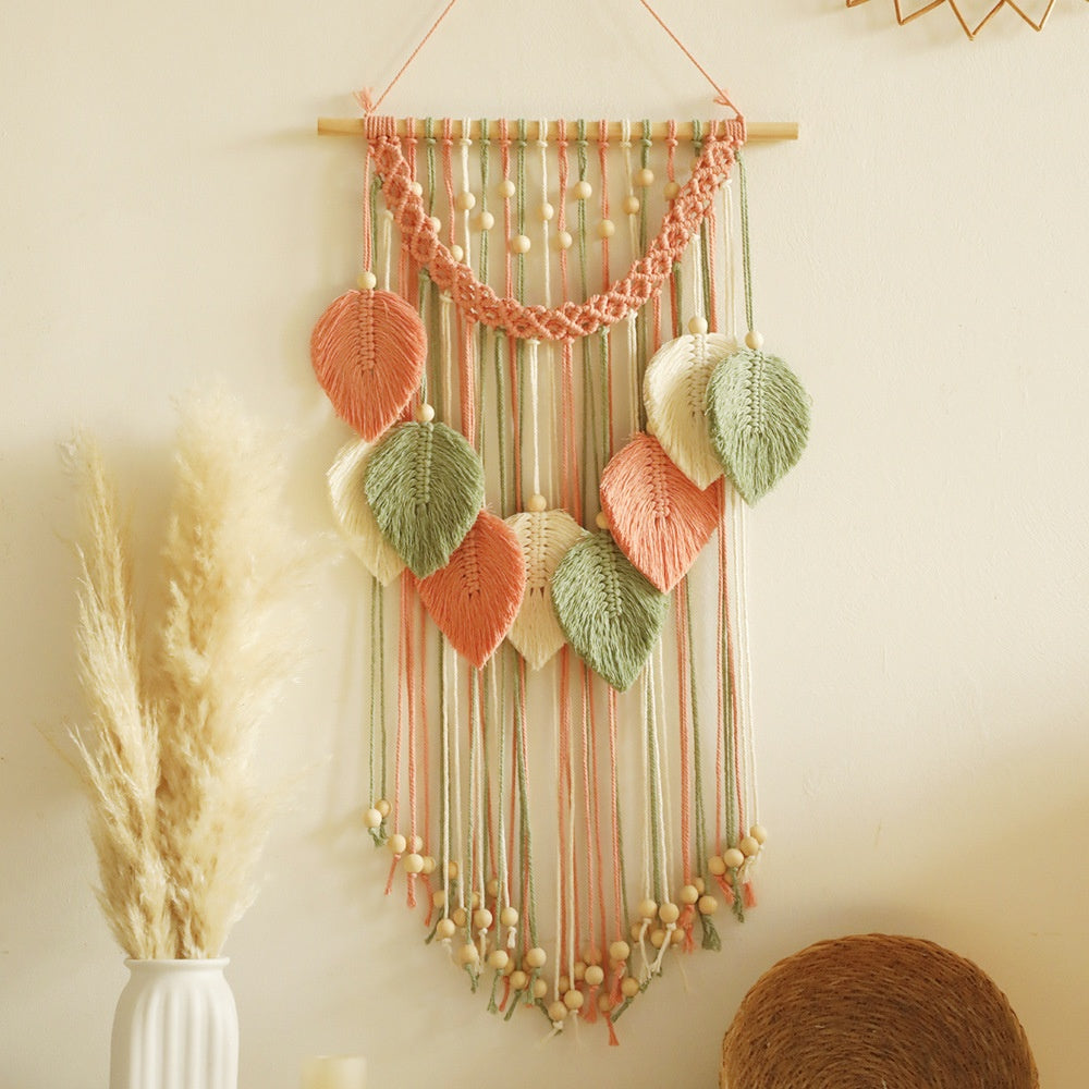 Decorative wall hanging with ribbons, leaves, and beads on a neutral background