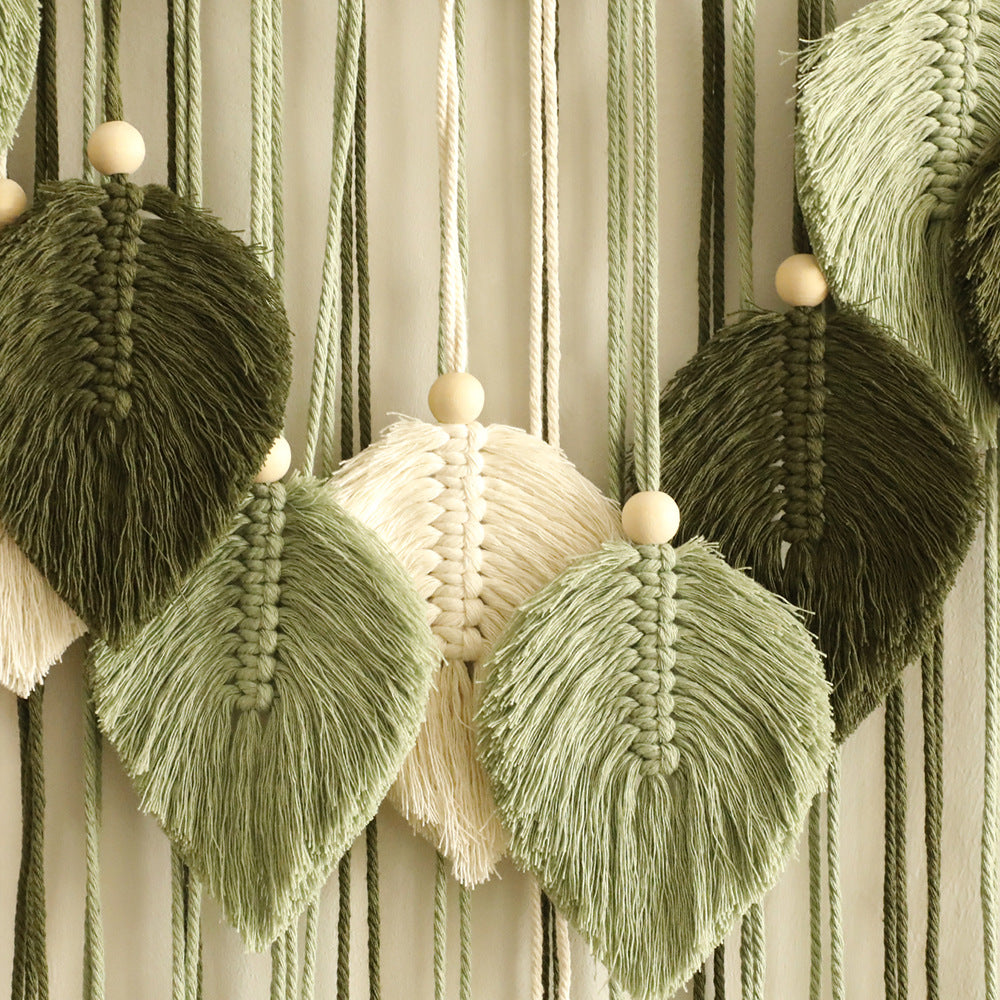 Macrame wall hanging with green, beige, and brown tassels on a striped background