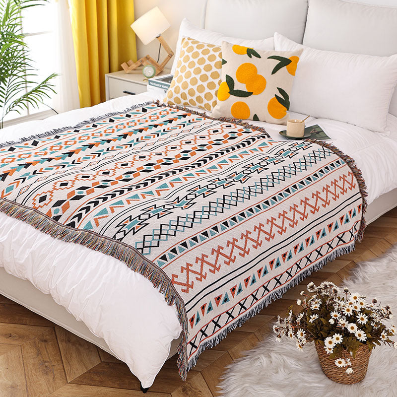 Patterned throw blanket on a bed with decorative pillows and a vase of flowers.