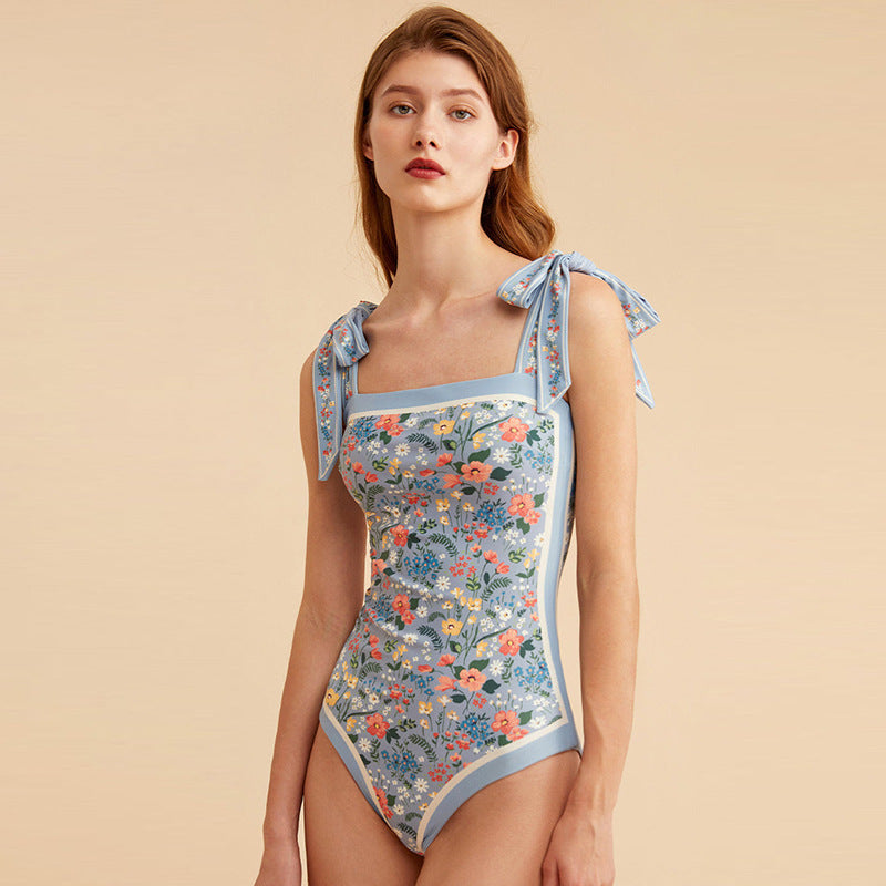 Woman wearing a floral one-piece swimsuit with tie straps on a beige background