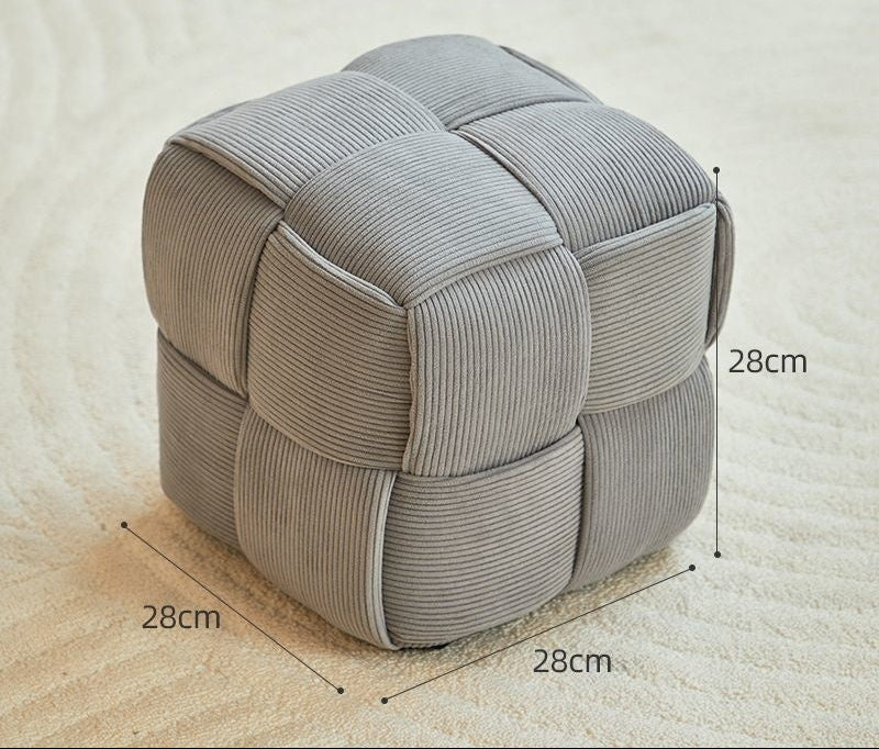 Light gray cube-shaped ottoman with measurements on a beige surface