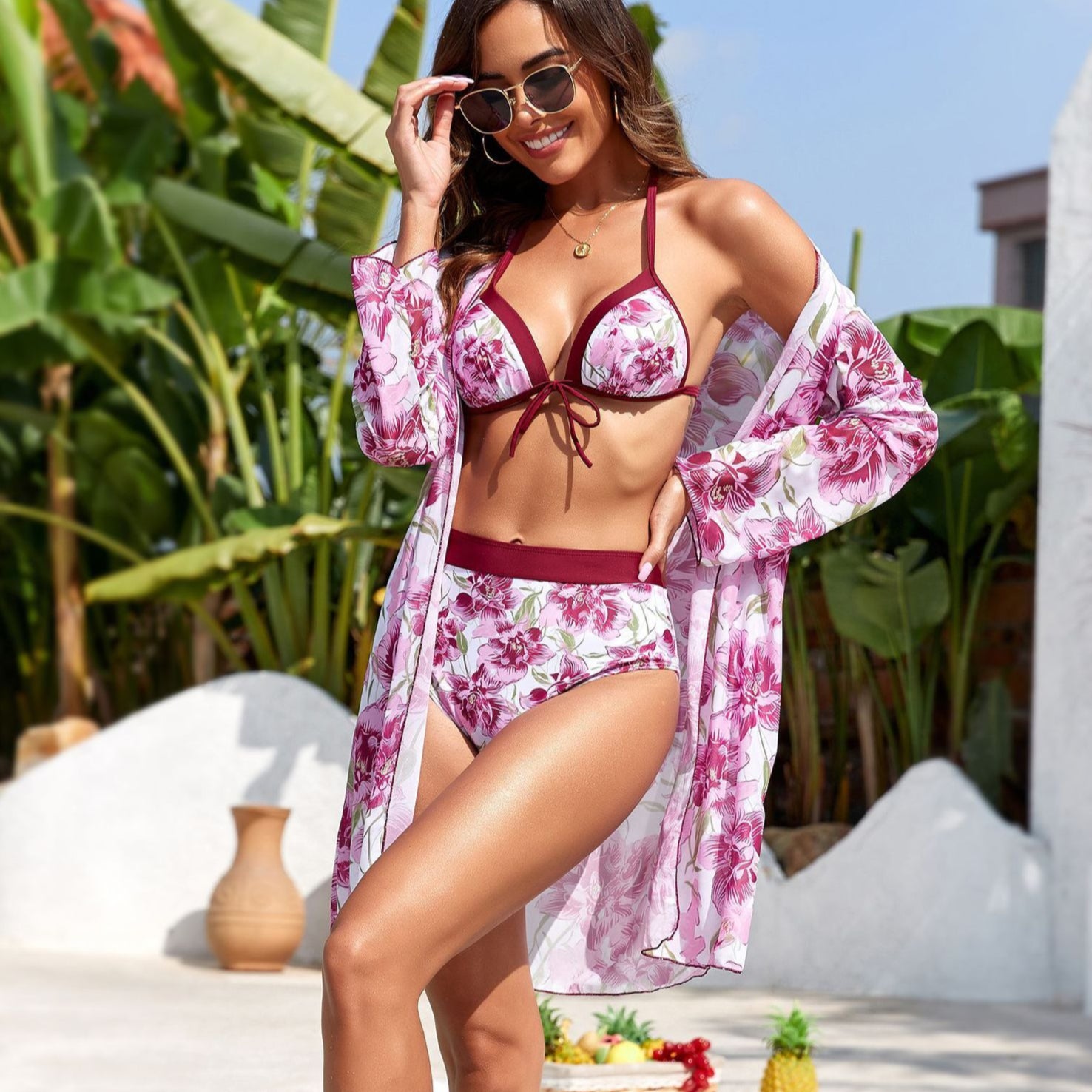 Woman in a floral bikini and cover-up standing by a pool with tropical plants in the background
