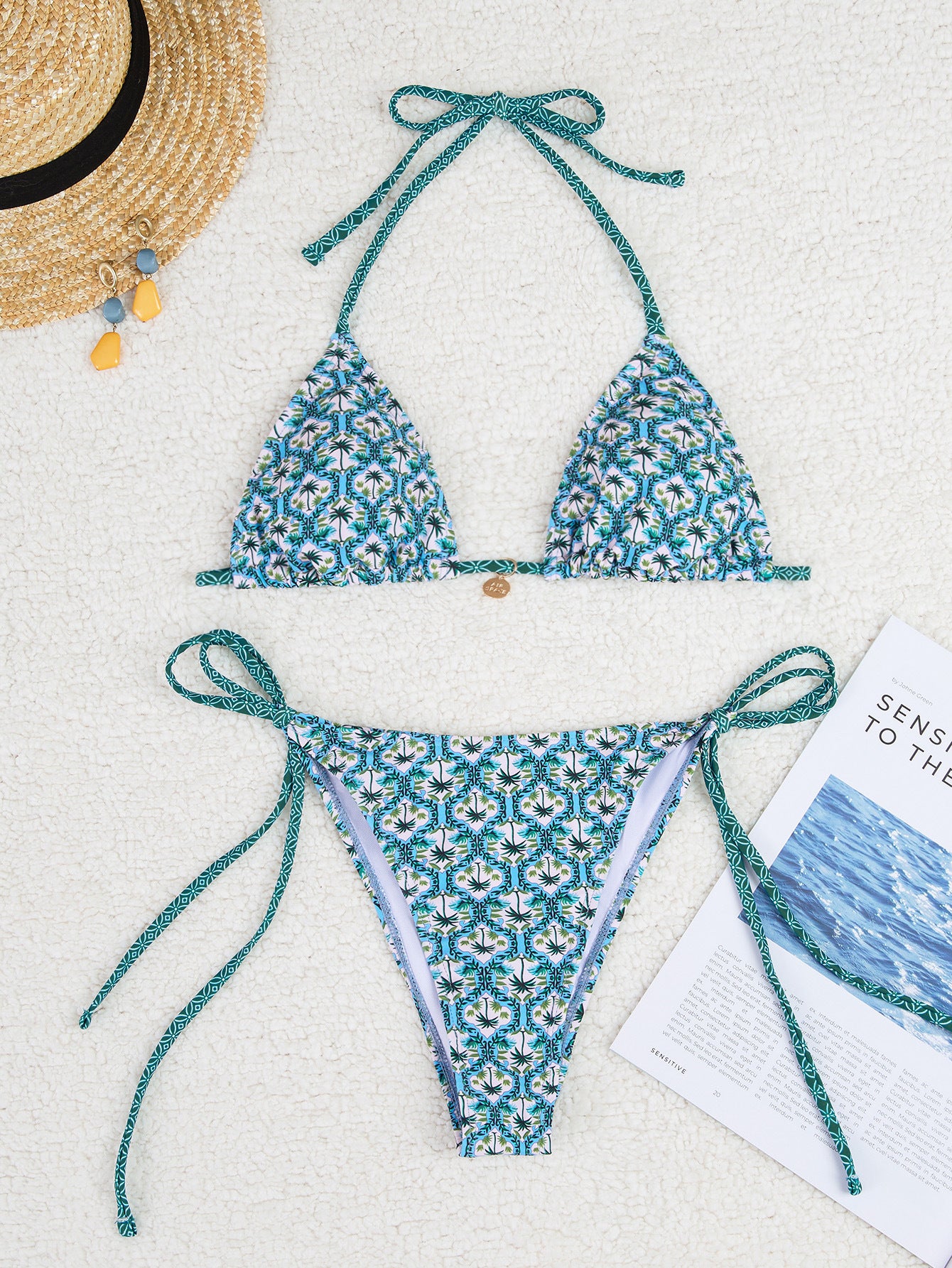 Blue floral bikini set on a white surface with a hat and magazine.