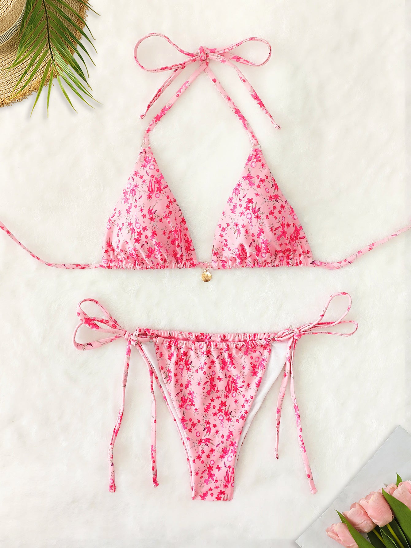Pink floral bikini set on a white surface with a straw hat and flowers.