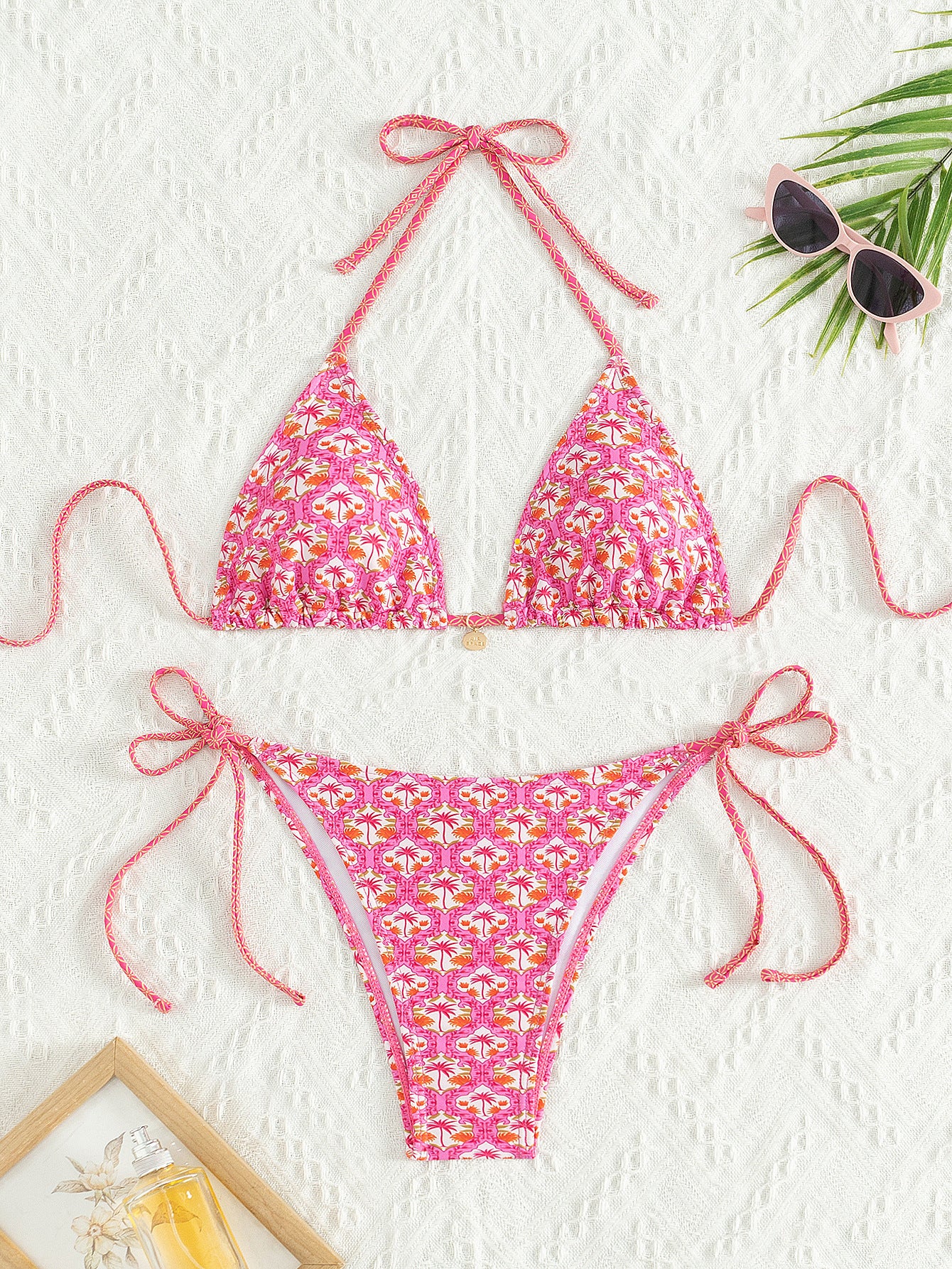 Pink floral bikini set on a white background with sunglasses and a palm leaf.
