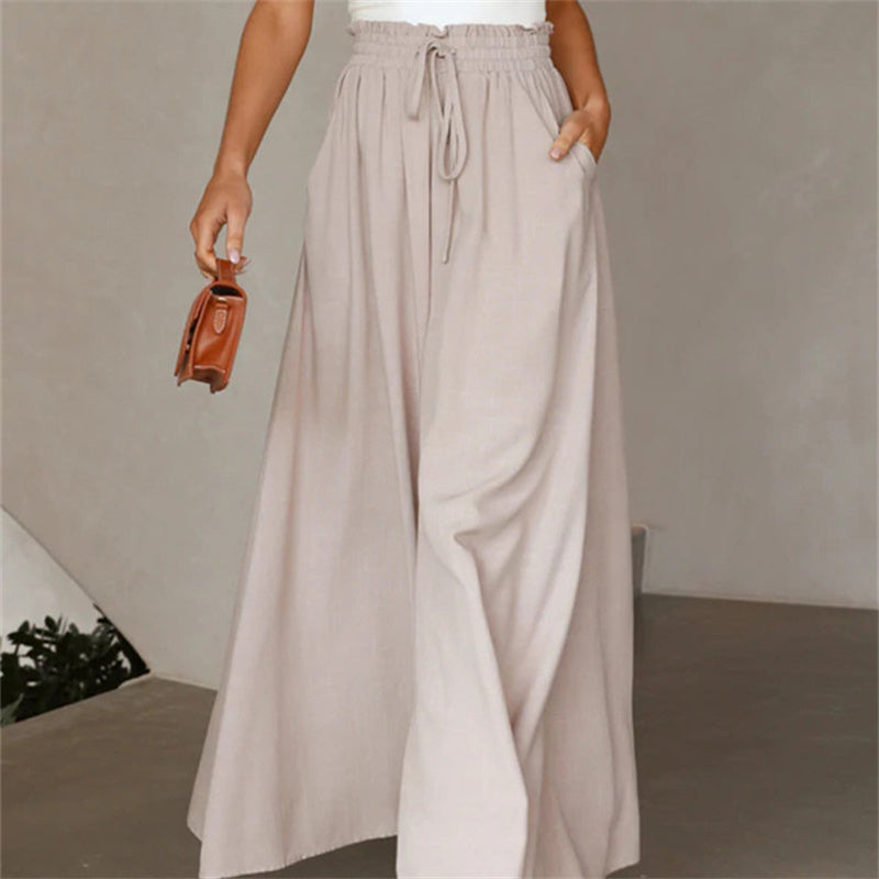 Person wearing beige wide-leg pants holding a brown handbag against a neutral background