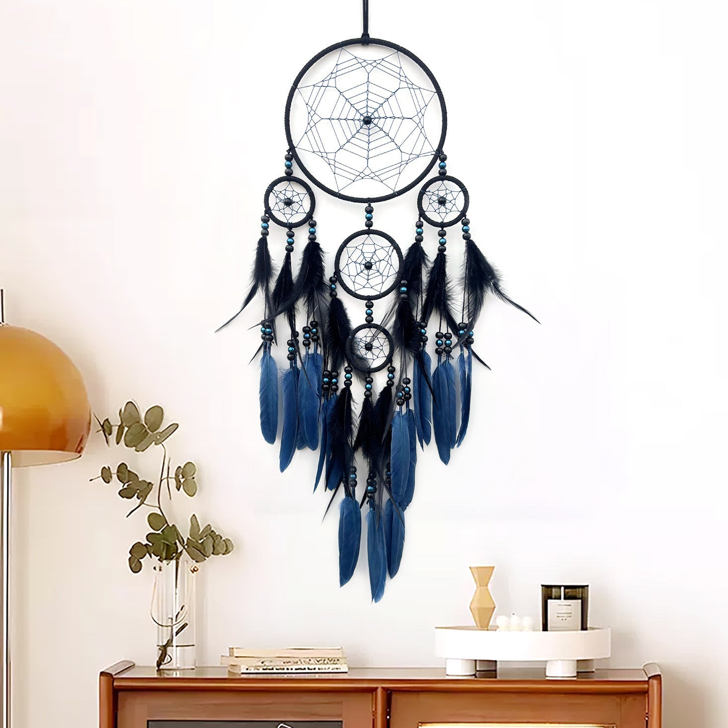 Black and blue dreamcatcher hanging on a white wall above a wooden cabinet.