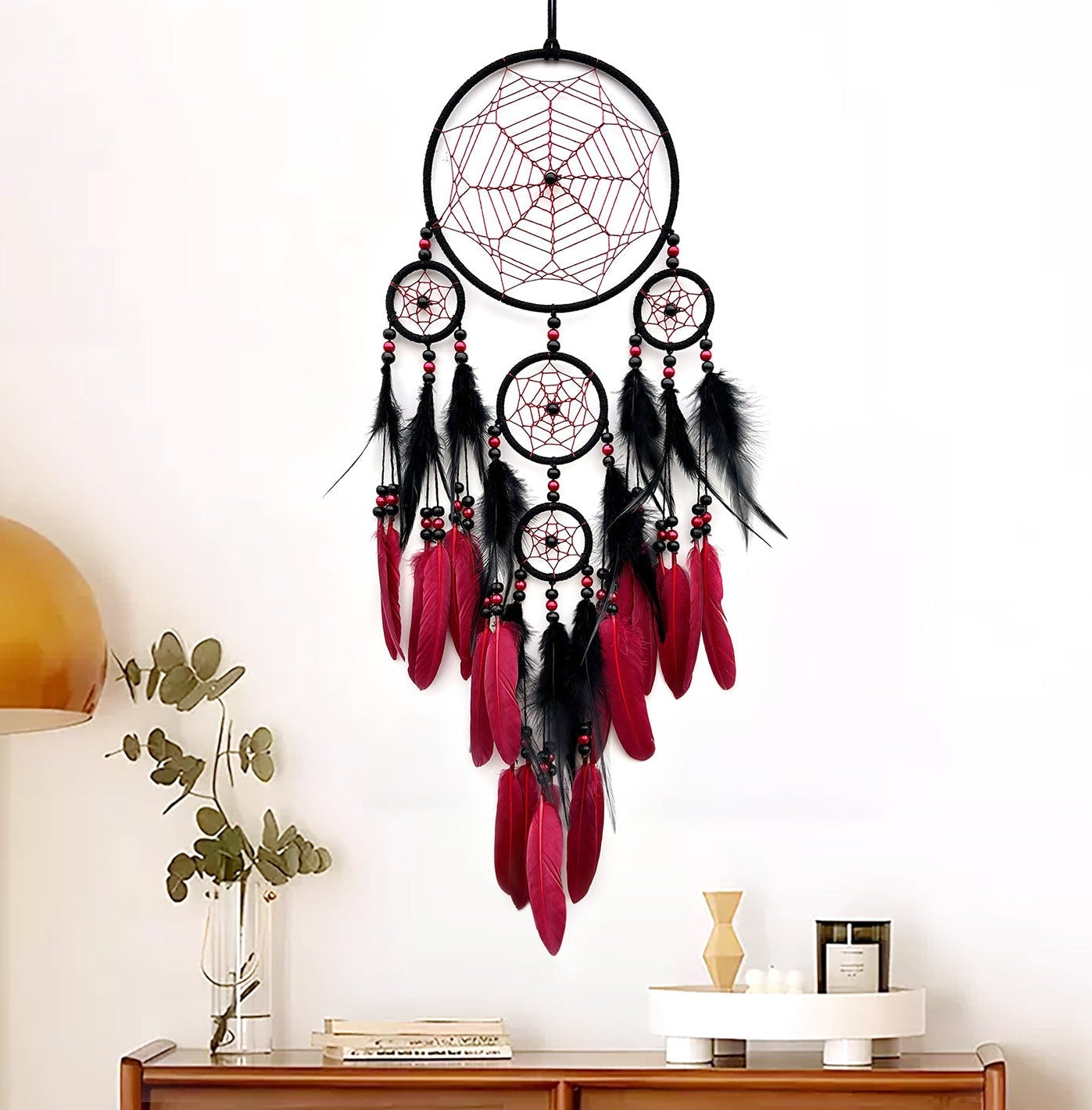 Dreamcatcher with red and black feathers hanging above a wooden cabinet.
